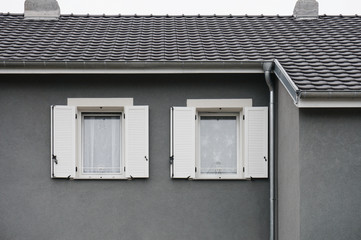Fototapeta na wymiar Holzfenster mit weißen PVC Klappläden in grauer Fassade