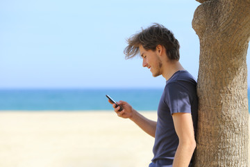 Side view of an attractive man using a smart phone on the beach