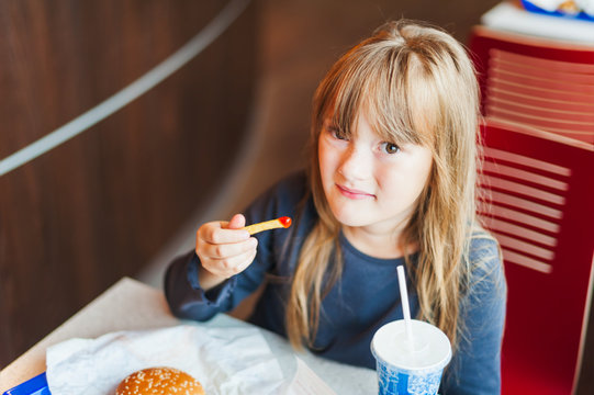 Little girl eating fast food in a cafe