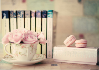 Vintage roses in a tea cup with macaroons and books