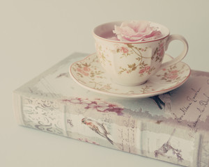 Vintage tea cup with a rose over an antique book - 74851490