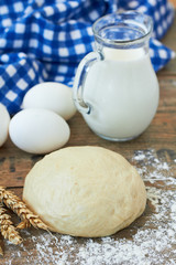 Dough, milk and eggs on a wooden table
