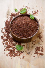 Raw red kernel rice in a wooden bowl, vertical shot