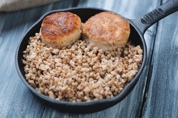 Cast-iron frying pan with meat cutlets and buckwheat, close-up