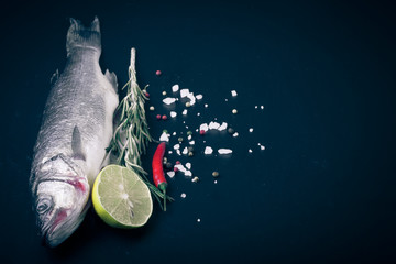 Fresh sea fish lying on dark background with spices. Space for t