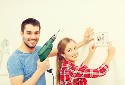 smiling couple drilling hole in wall at home