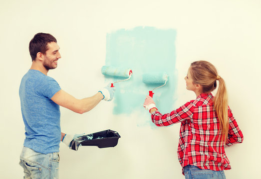smiling couple painting wall at home