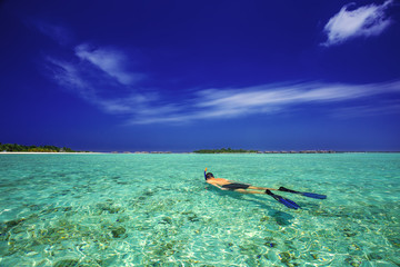 Young man snorkling in tropical lagoon with over water bungalows