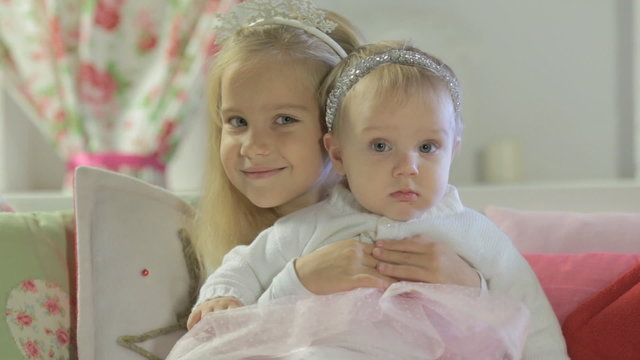 Little cute girl sitting on couch and hugging her little sister