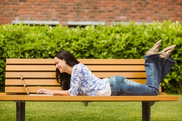 Cool brunette lying on bench using laptop