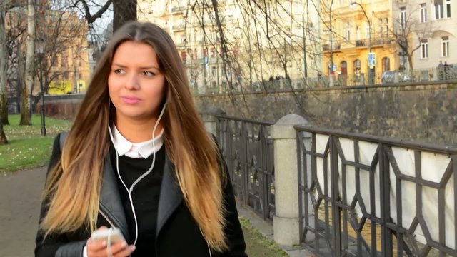 young attractive woman walking and listens music on smartphone