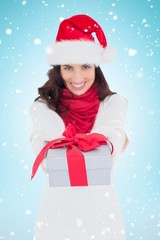 Composite image of festive brunette in santa hat giving gift