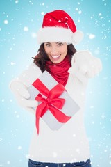 Composite image of excited brunette in santa hat giving gift