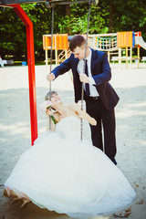 beautiful young wedding couple in park, blonde bride on swing an