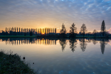 Fototapeta premium Winter sunset in the shore of a lake with clouds reflected in th