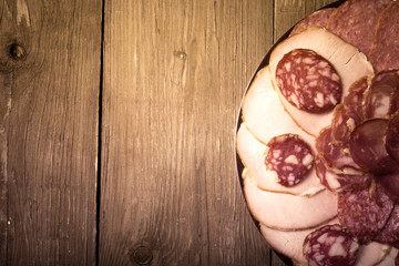 plate with different sliced sausage on an old wooden table. With