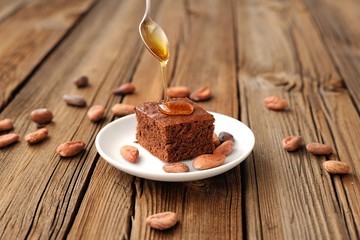 Chocolate cake with cocoa beans and honey on wooden background
