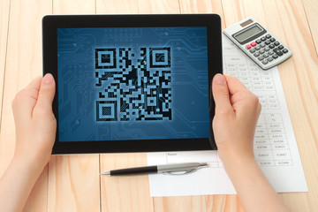Hands hold tablet PC with QR code on wooden background .