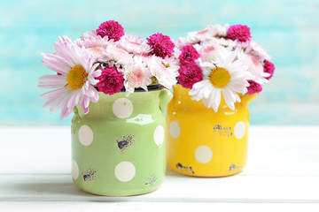 Beautiful flowers in cans on table on light blue background