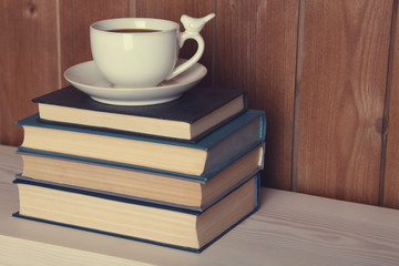 Pile of books with cup on tabletop and wooden background