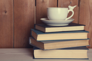 Pile of books with cup on tabletop and wooden background