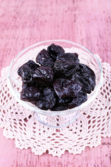 Prunes in glass bowl on lace doily on color wooden background