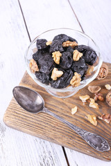 Wooden board with glass bowl of prunes and walnuts, shell and