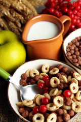 Various sweet cereals in ceramic bowls, fruits and jug with