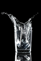 Water splash with ice in glass isolated on black