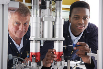 Engineer And Apprentice Working On Machine In Factory