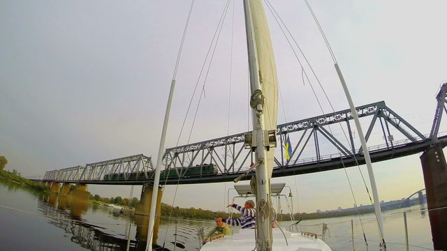 Tourist yacht sailing under river railway bridge, moving train 