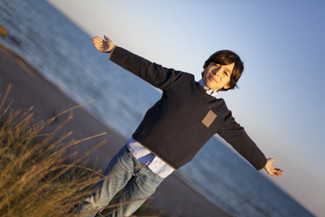 Niño con brazos en cruz con mar de fondo