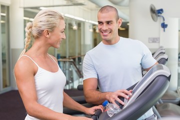 Fototapeta na wymiar Trainer assisting woman with treadmill screen options at gym