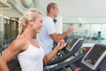 Fototapeta na wymiar Side view of couple running on treadmills at gym