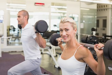 Fototapeta na wymiar Sporty young couple lifting barbells in gym