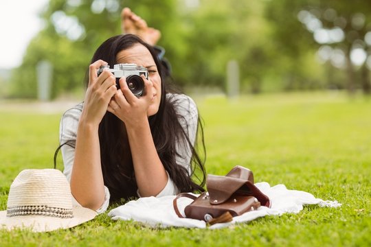 Brunette lying on grass taking picture