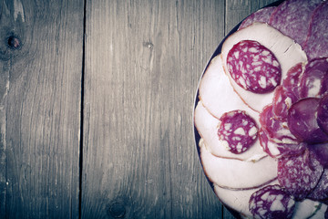 plate with different sliced sausage on an old wooden table. With