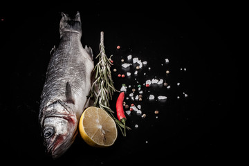 Fresh sea fish lying on dark background with spices. Space for t