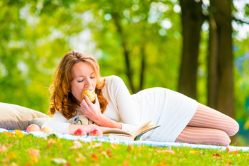 Red-haired student eats an apple and reading books in the park