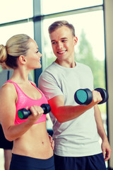 smiling young woman with personal trainer in gym