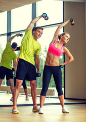 Naklejka premium smiling man and woman with dumbbells in gym
