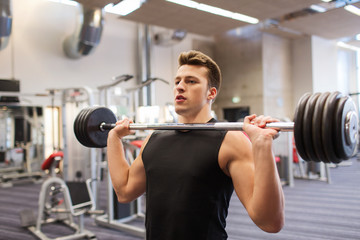 young man flexing muscles with barbell in gym