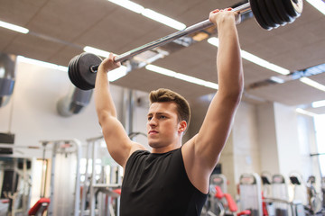 young man flexing muscles with barbell in gym