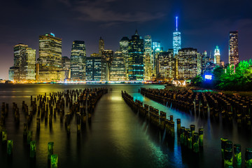 Pier pilings and the Manhattan skyline at night, seen from Brook