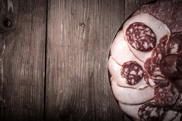 plate with different sliced sausage on an old wooden table. With