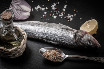 Fresh sea fish lying on dark background with spices.
