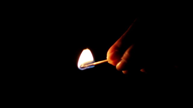 Burning match in woman's hand on black background