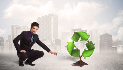 Business man watering green recycle sign tree on city background