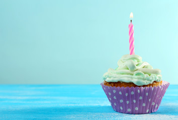 Delicious birthday cupcake on table on light blue background