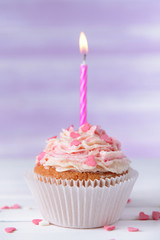 Delicious birthday cupcake on table on light purple background